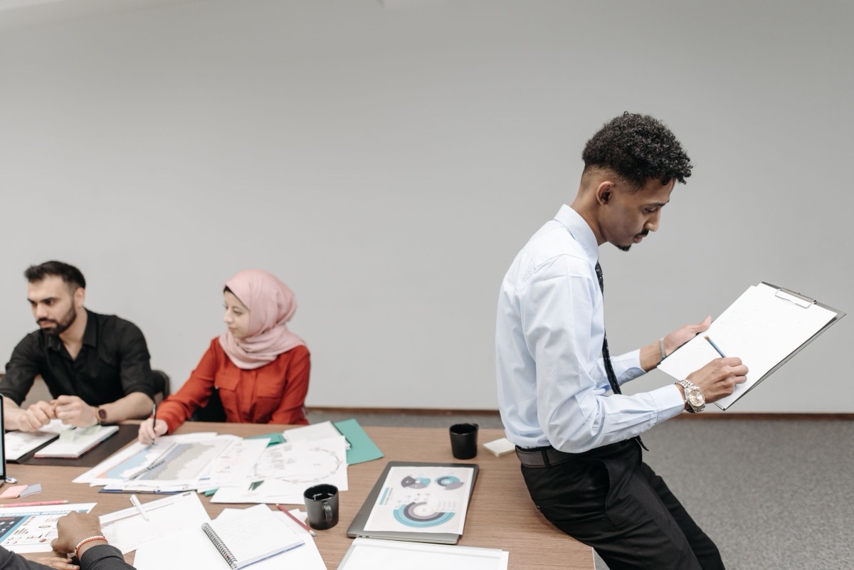 Colleagues at a meeting table with printed charts and papers while one man looks at a clipboard