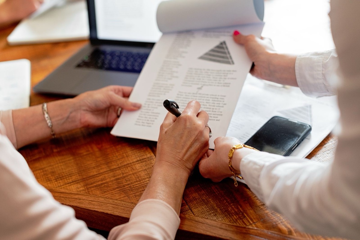 Two people at a wooden table going through a printed page with a pyramid diagram, beside a phone