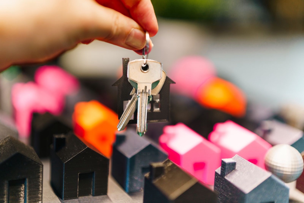 A hand holding a set of keys above small model houses on a table
