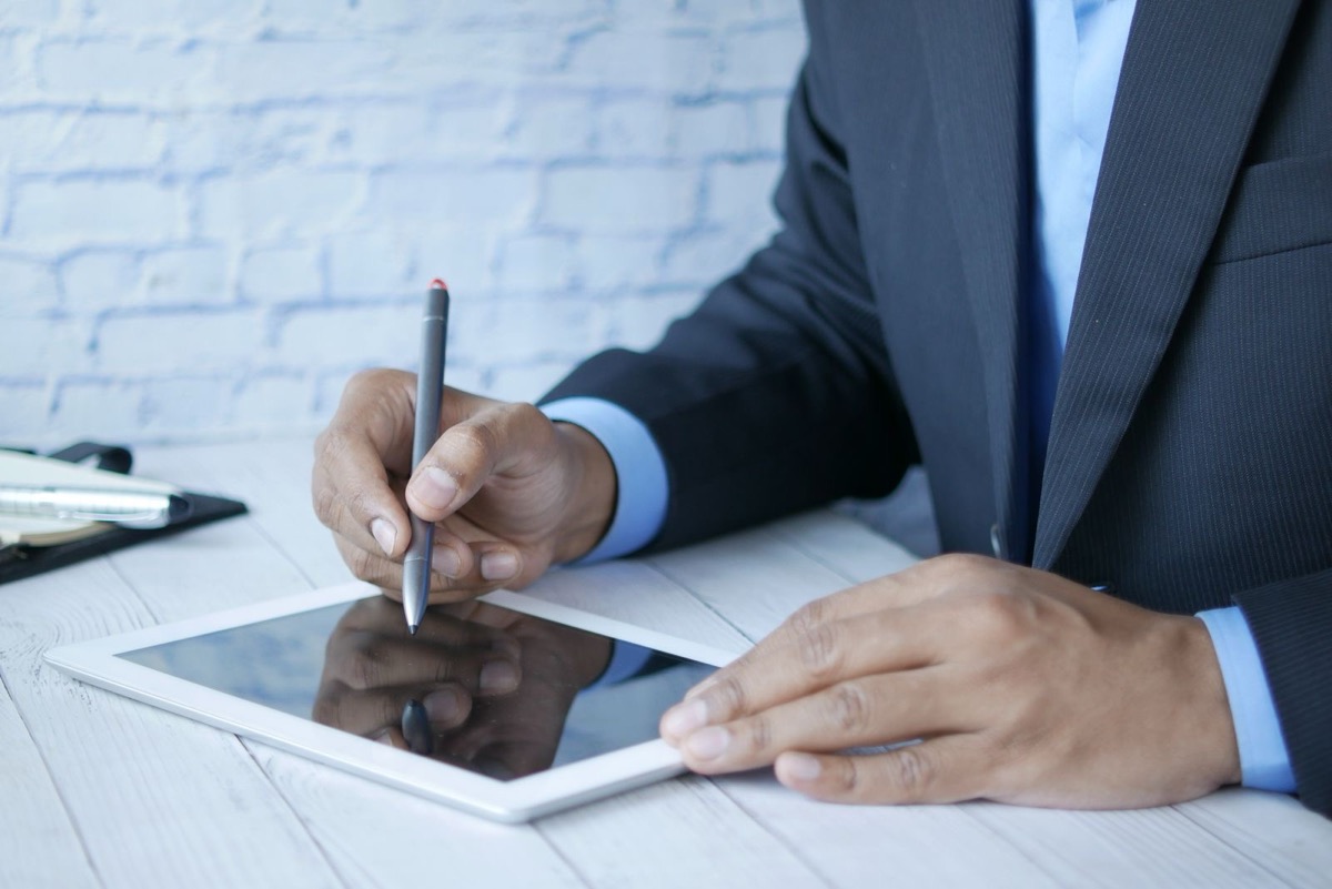 A person in a dark suit writing on a tablet with a stylus at a white desk