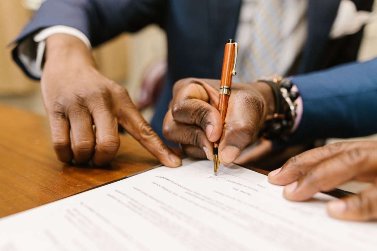 Hands signing a printed document with an orange pen at a wooden table